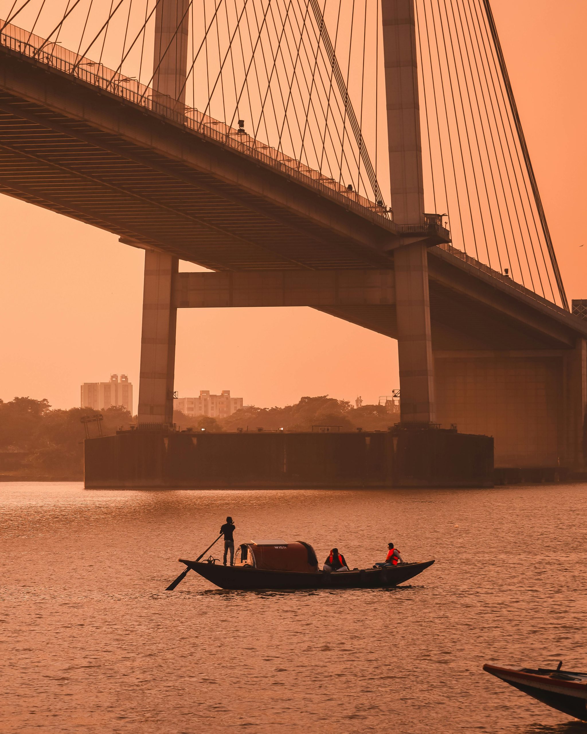 Boat with people underneath Vidyasagar Setu during sunset on Hooghly River, Kolkata.
